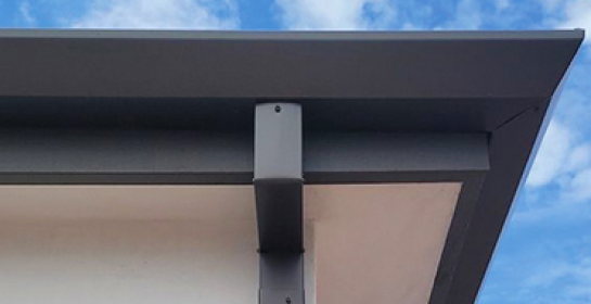 Aquasoltech seamless aluminum rain gutter and downspout detail on a residential roof edge in San Diego, showing a clean, modern rainwater management system against a partly cloudy sky.