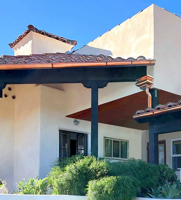 Aquasoltech finished exterior project in San Diego featuring copper‑tone seamless gutters installed along a Mediterranean‑style home roofline with wooden support beams and lush landscaping.